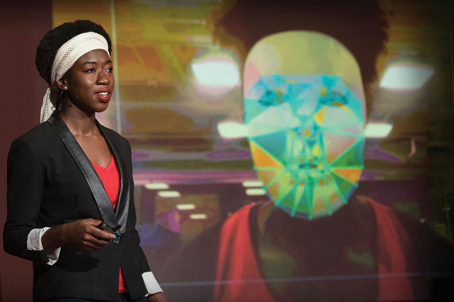 Joy Buolamwini, a dark-skinned woman with short dark hair, stands in front of a demonstration of facial recognition software.
