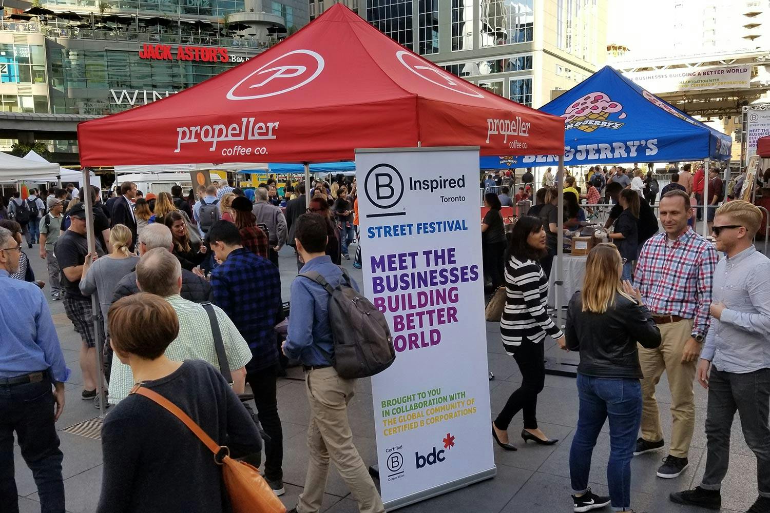 Canopy tents of various brands in a crowded plaza. A pull-up banner reads “Meet the businesses building a better world.”