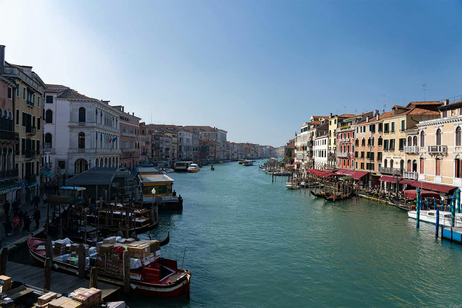 The grand canal in Venice extends into the distance, flanked by earth-toned buildings boats docked in front of them.