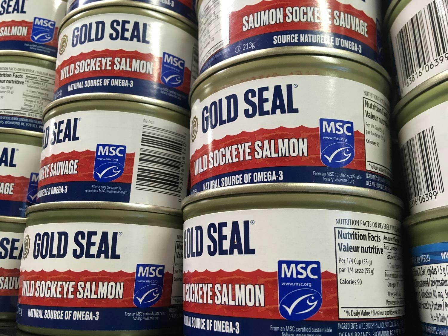 Stacked cans of Gold Seal wild sockeye salmon. Each can has a blue MSC label bearing a small white emblem of a fish.