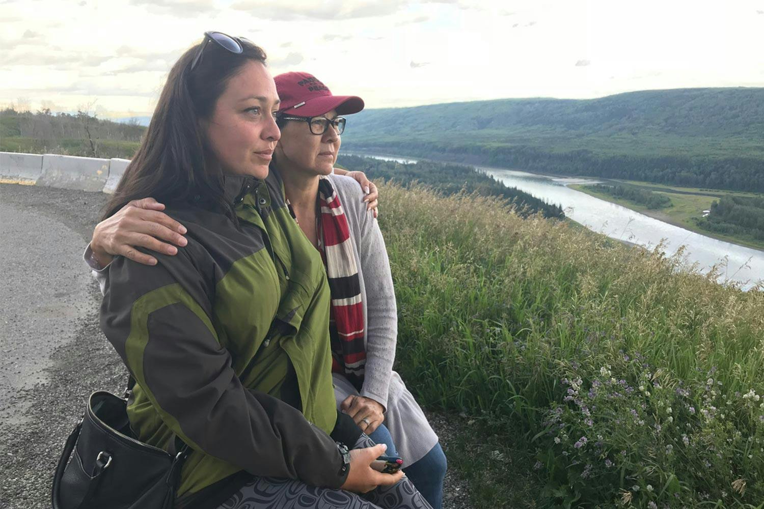 Heather Hatch and Diane Abel sit together, embracing each other by the shoulder, atop a hill overlooking the Peace River.