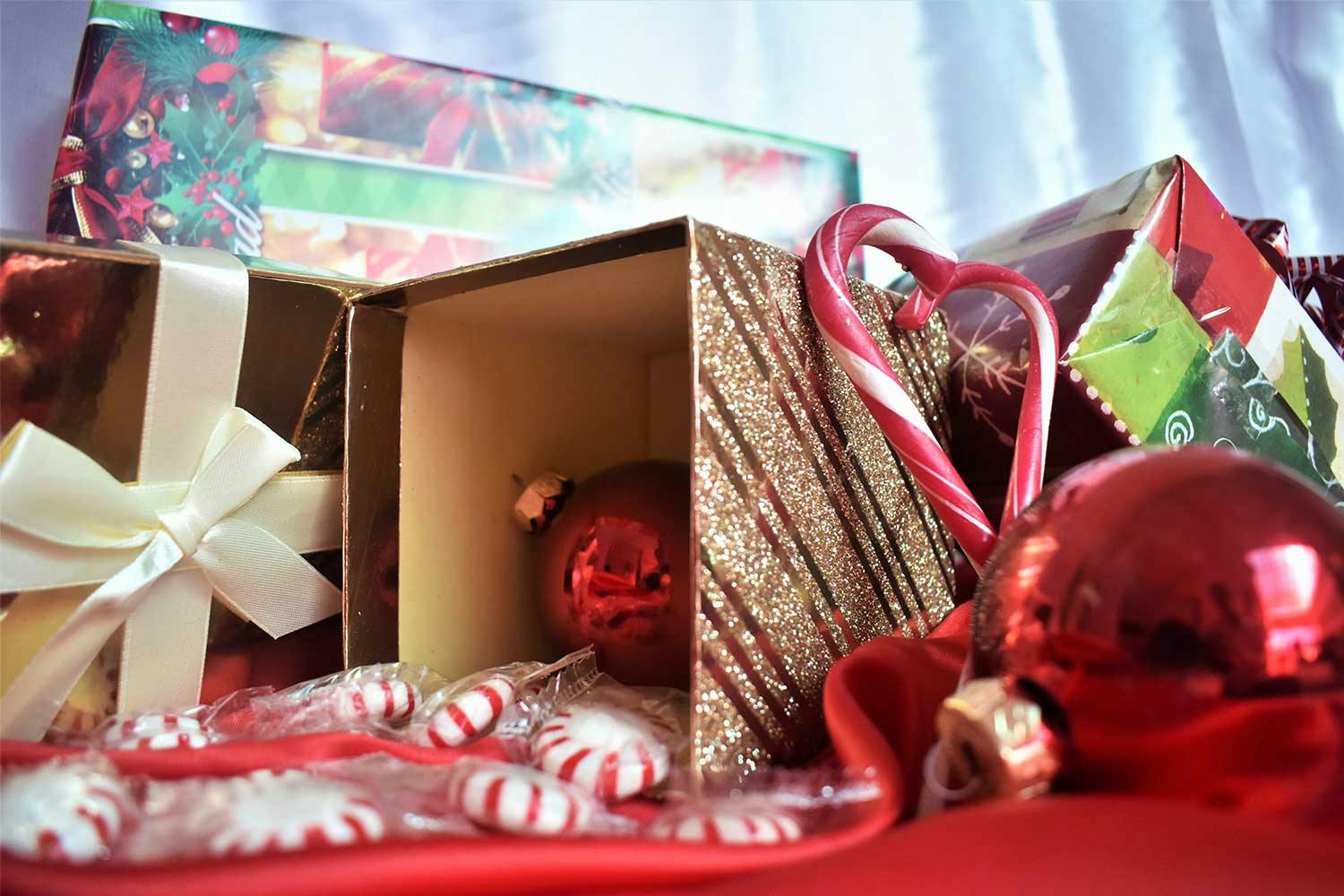 Red tree ornaments, plastic-wrapped mints, candy canes, and paper-wrapped & glitter-covered gift boxes arranged in a pile.