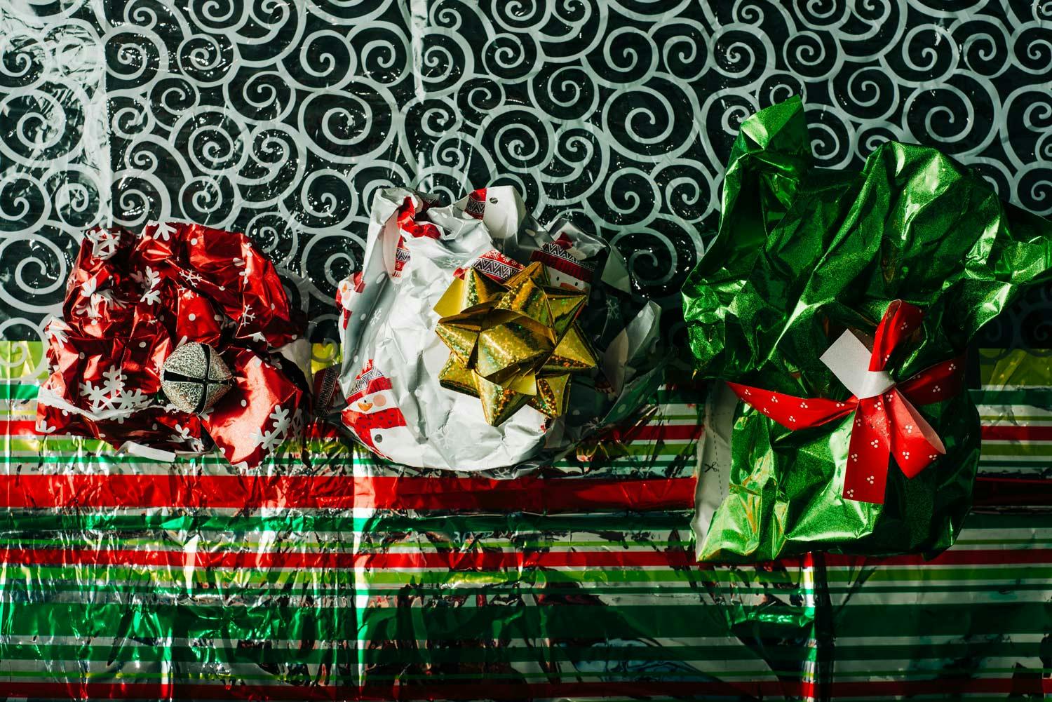 3 crumpled balls of wrapping paper topped with a bell, a star & a ribbon on a sheet of wrapping paper with swirls & stripes.