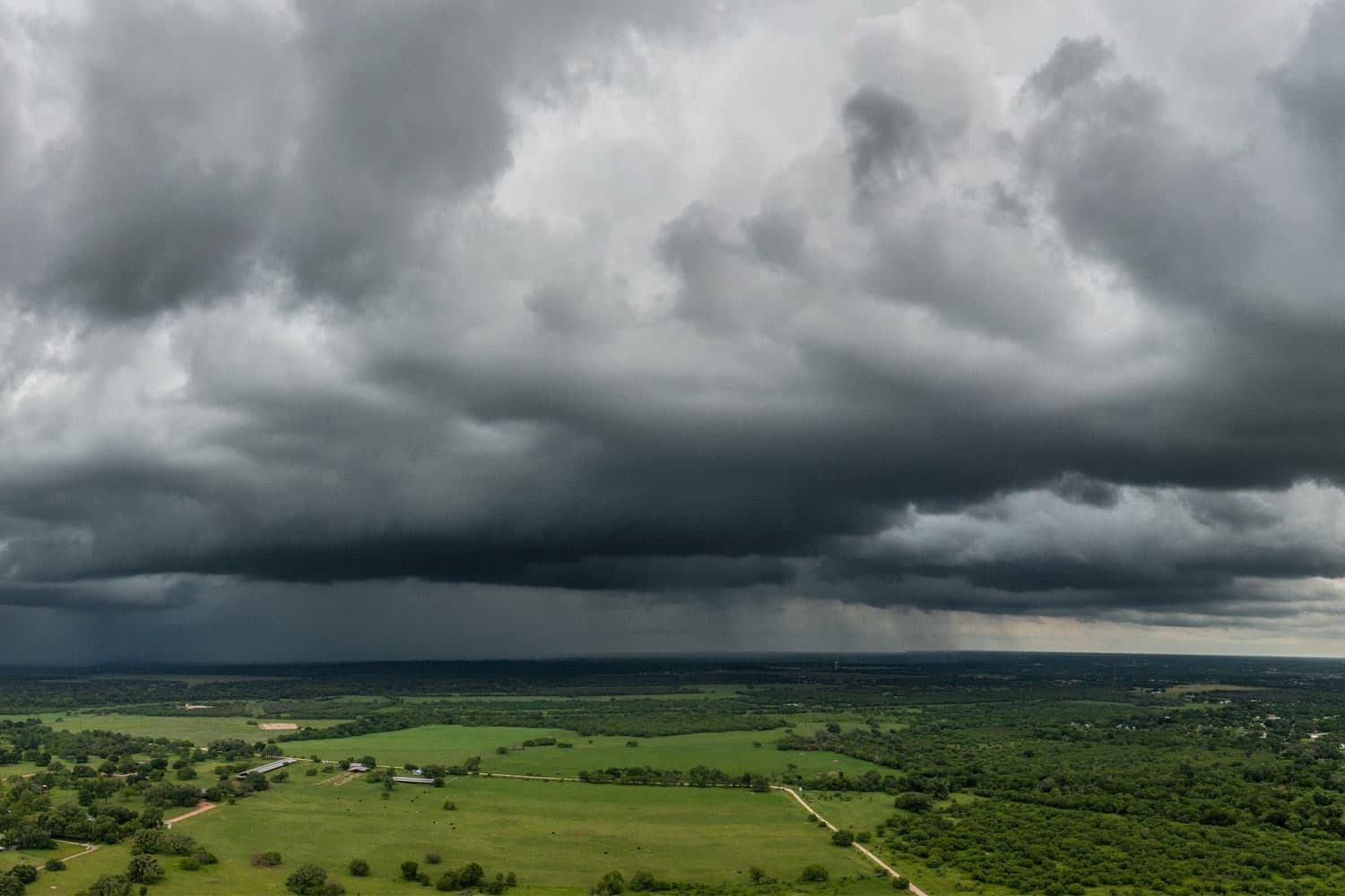 Ominous, dark grey stormclouds hang over green farmland dotted with trees.