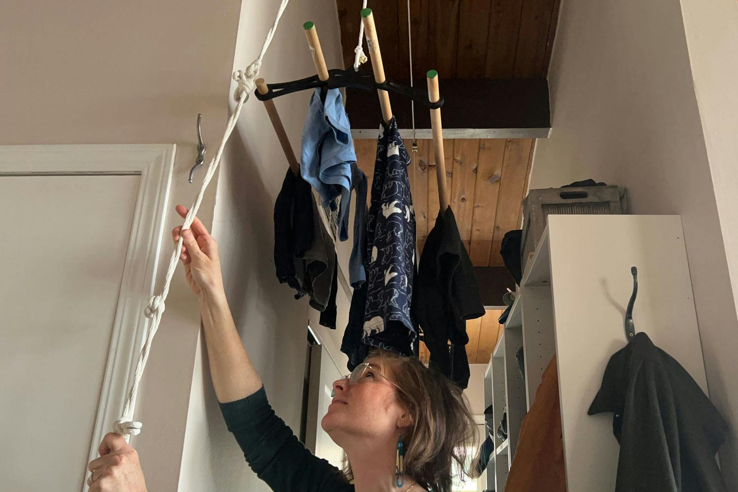 A woman pulls on a rope attached to a ceiling-mounted drying rack in the hallway of her home.