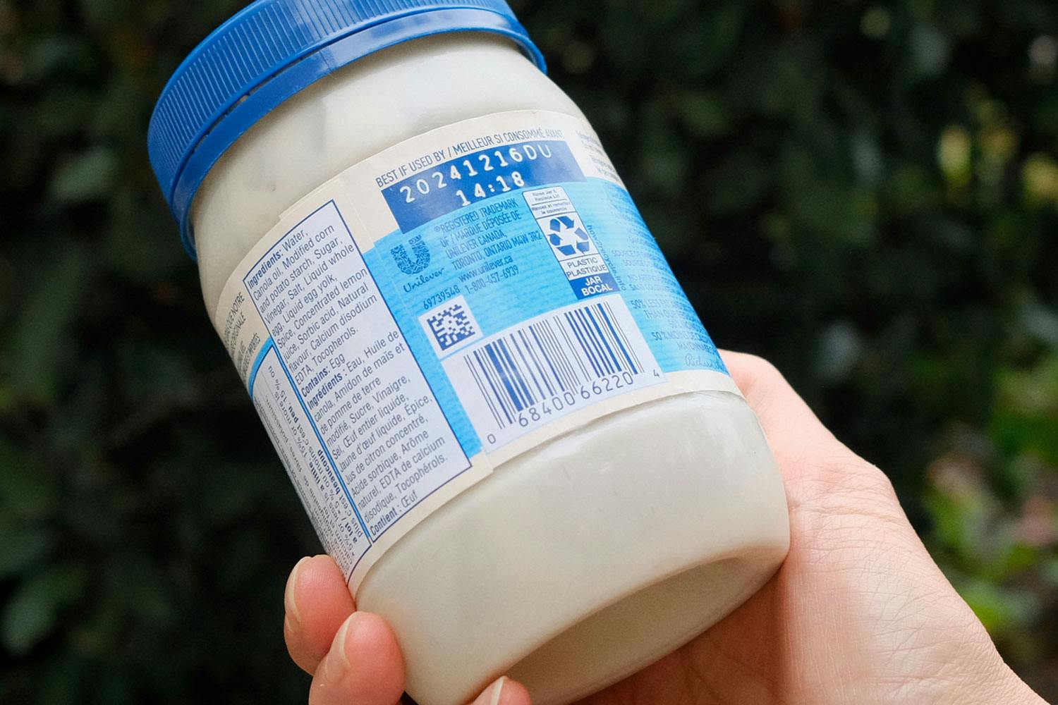 A light tan-skinned hand holding a jar of mayonnaise showing the best before date.