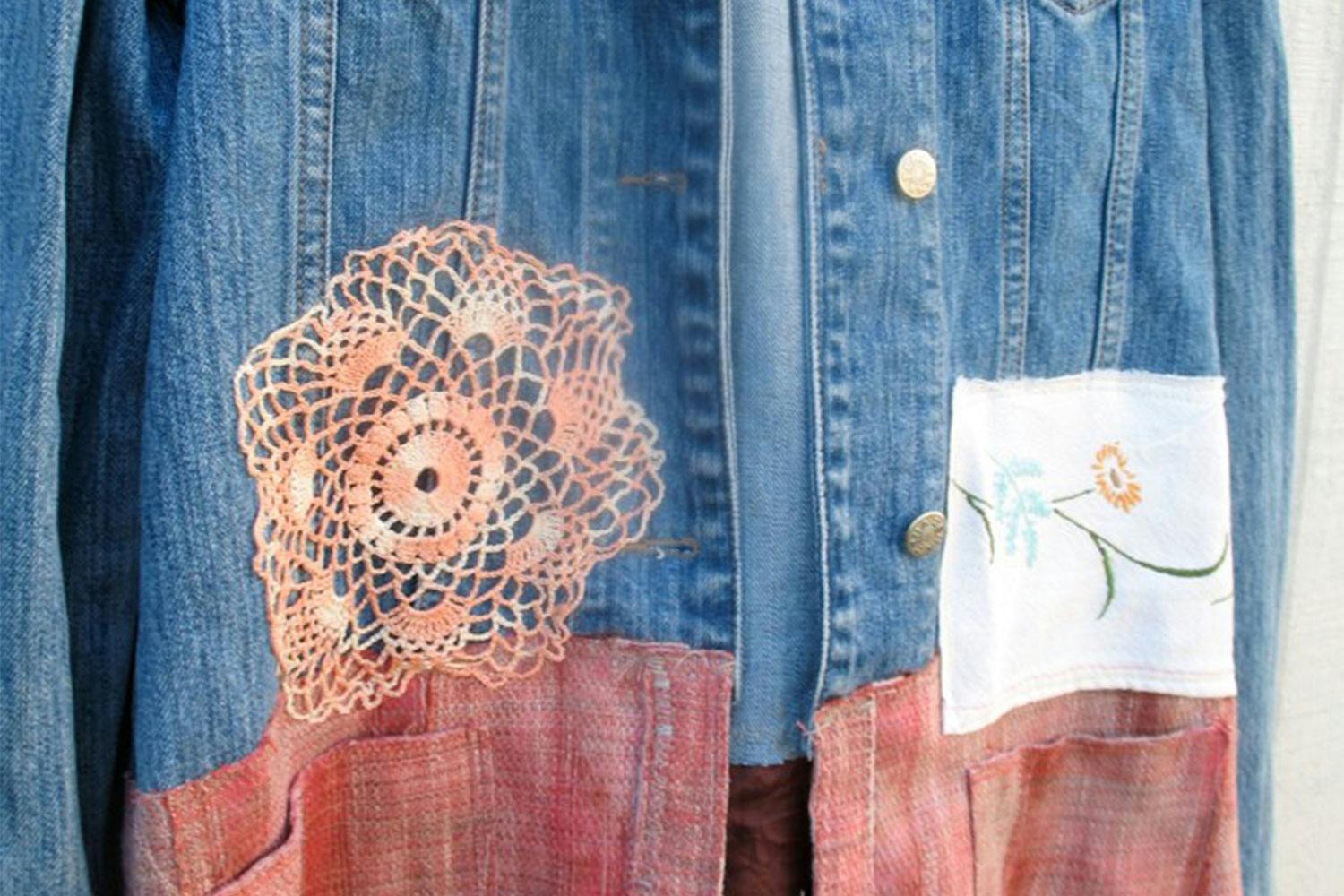 A jean jacket customized with red lower half, an orange flower patch, and a white square patch embroidered with flowers.