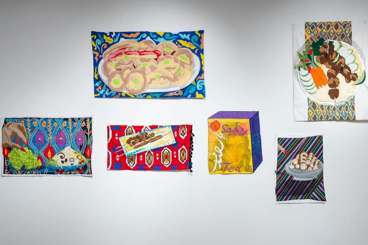 6 Hangama Amiri quilts hang on a white gallery wall. They each depict different Afghan foods.