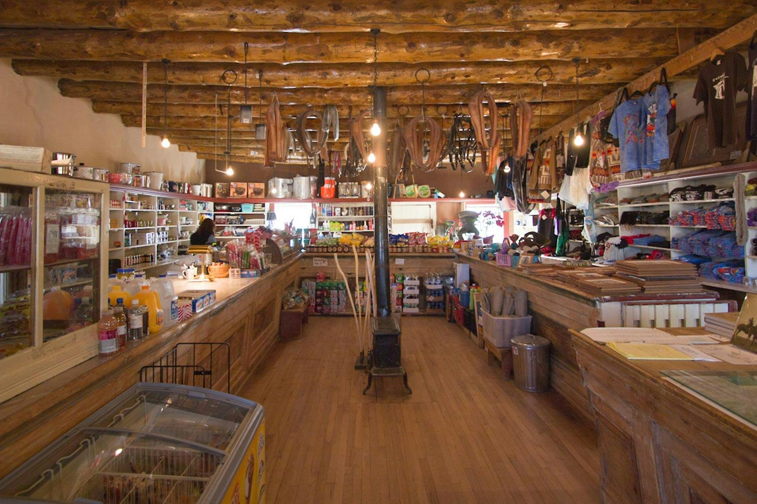Interior of a trading post. Leather goods hang from log rafters. Souvenir shelves and a wooden counter wrap around the room.