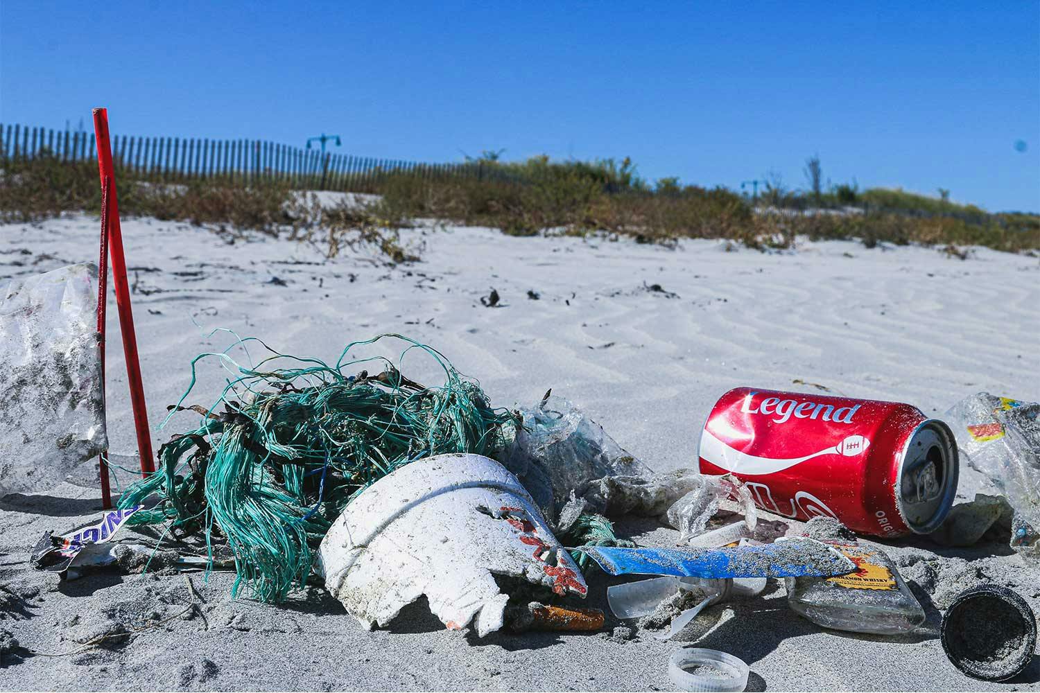 Blue fishing line, styrofoam, a coke can, candy wrappers, and other garbage washed up on a sandy beach.