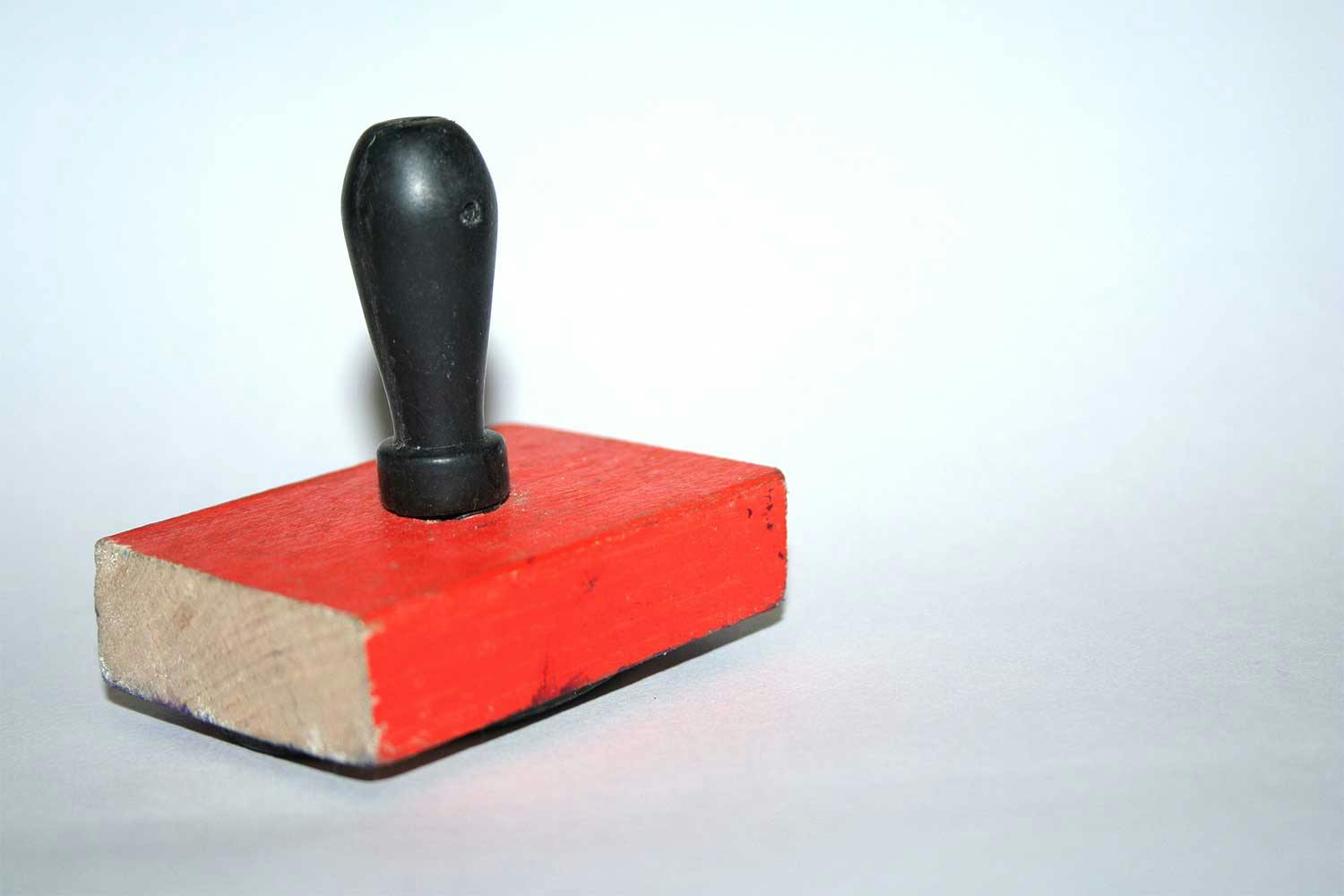 A rubber stamp comprising a wooden block painted red topped with a bulbous black handle.
