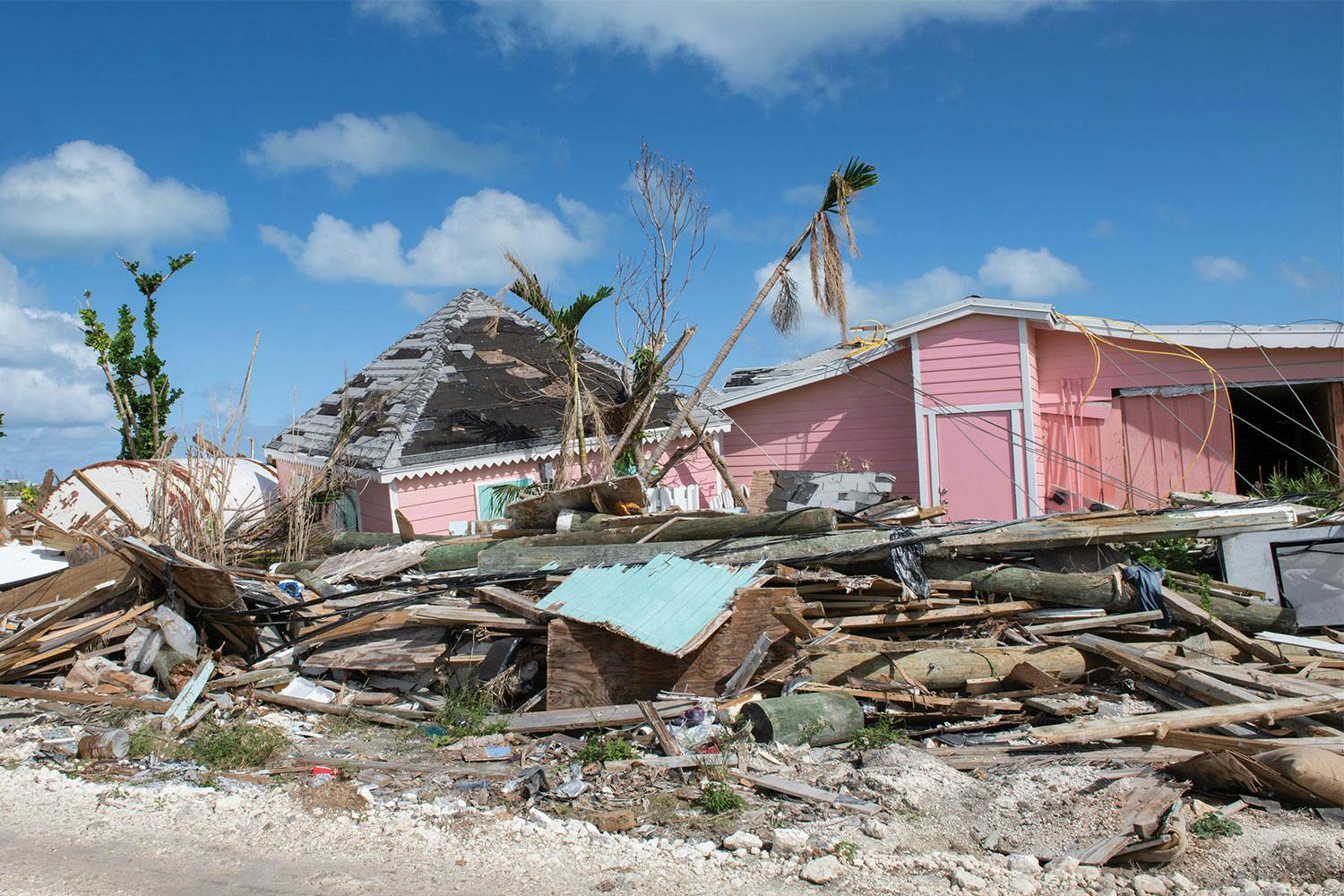 The rubble of a house destroyed by Hurricane Dorian in front of a still partly standing pink house in The Bahamas.