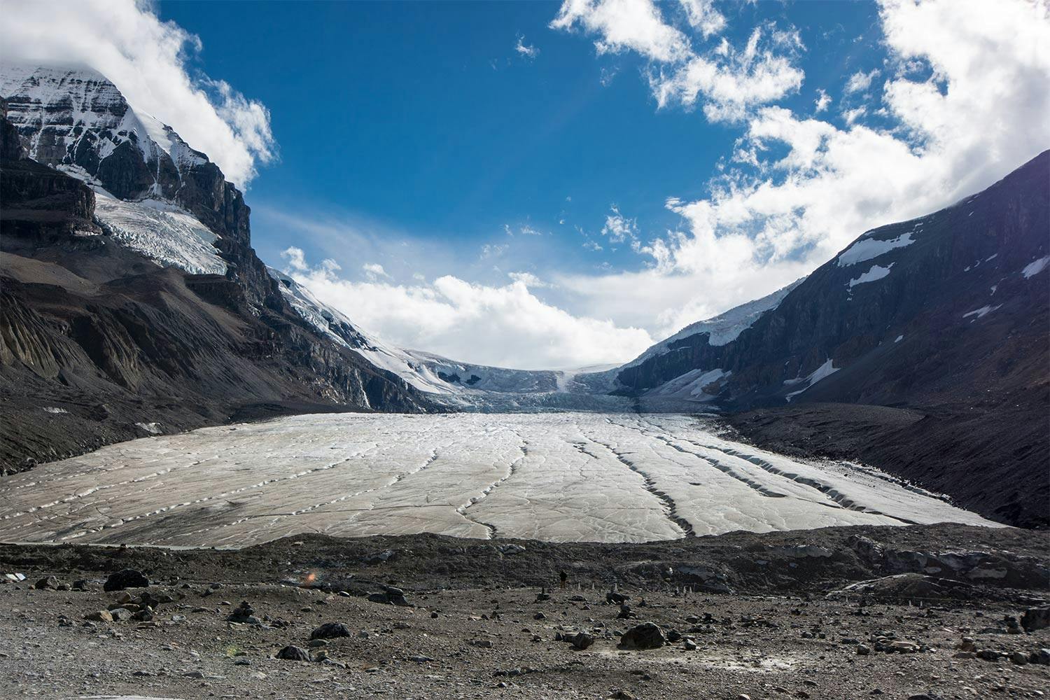 Under a blue sky, glacial ice extends into the distance between two immense mountains in Alberta's Athabasca Glacier.