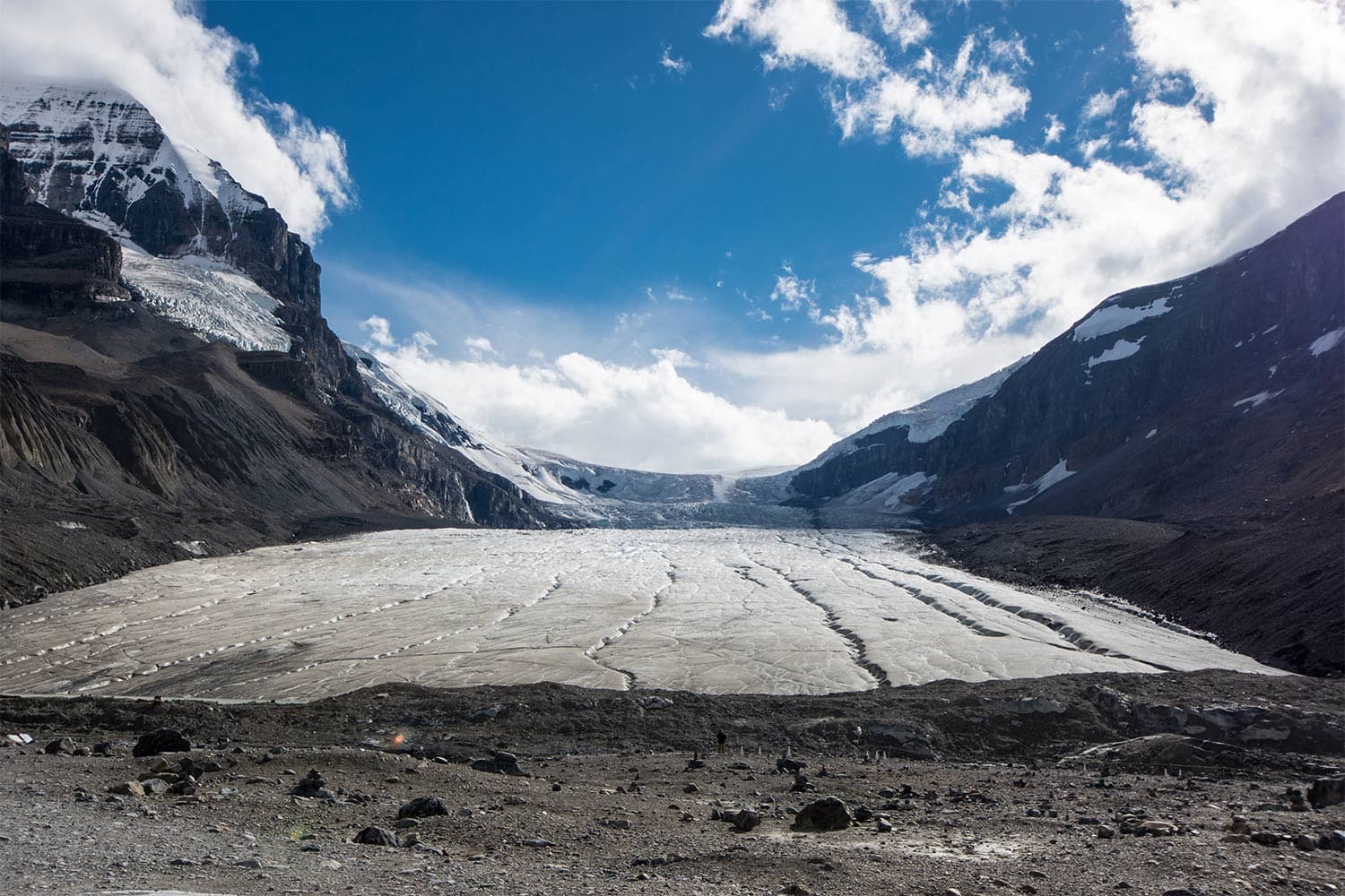 Under a blue sky, glacial ice extends into the distance between two immense mountains in Alberta's Athabasca Glacier.