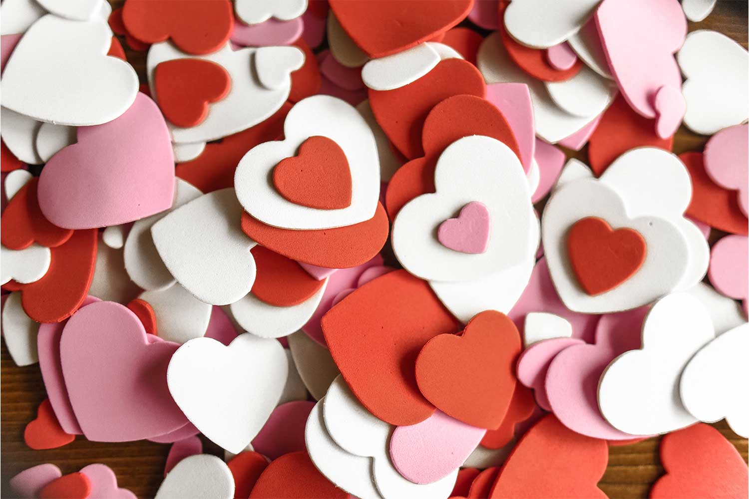 A pile of pink, red, and white foam hearts on a wooden tabletop.