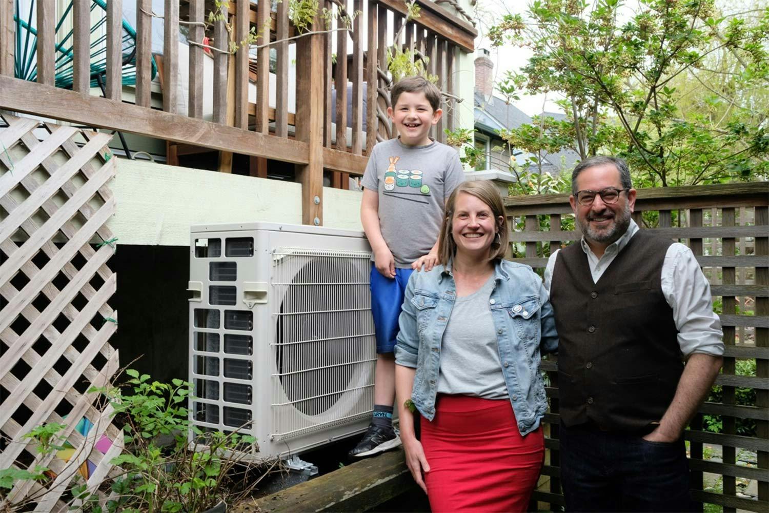 From R to L: Seth Klein, Christine Boyle and their son Aaron stand beside their heat pump in ther backyard, under the porch.