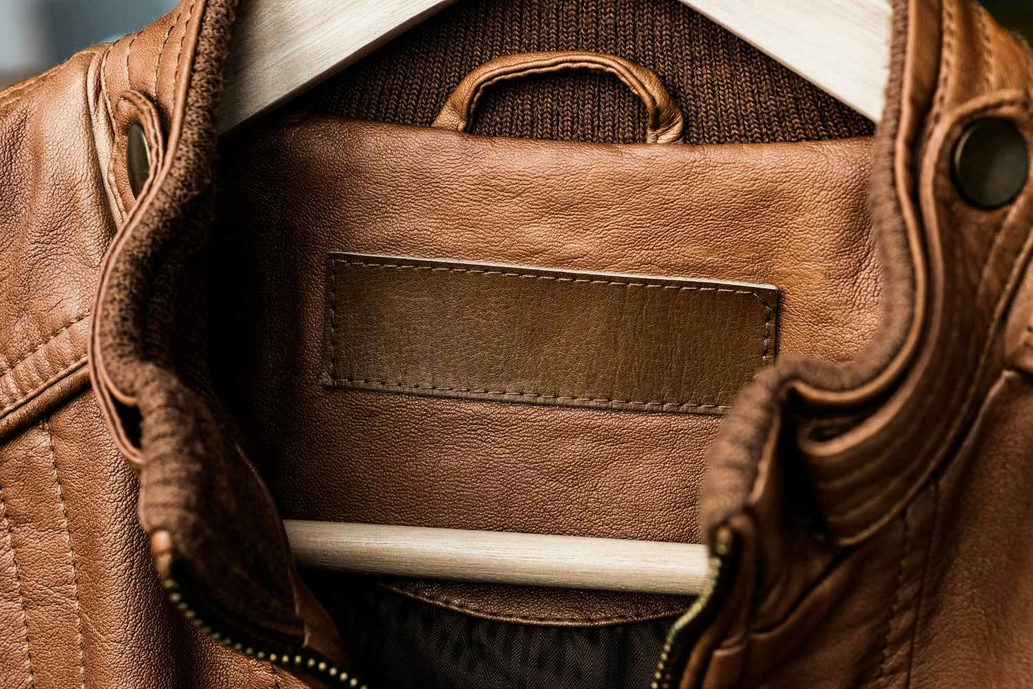 Close-up of a rectangular, dark brown leather patch on the interior neck area of a brown leather jacket.