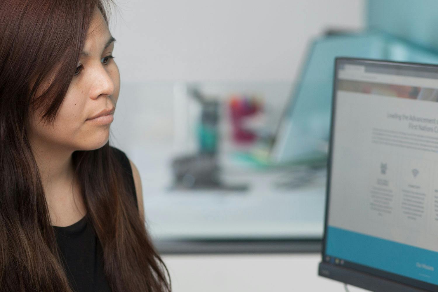 A woman with light brown skin and reddish-brown hair looks at a computer monitor.