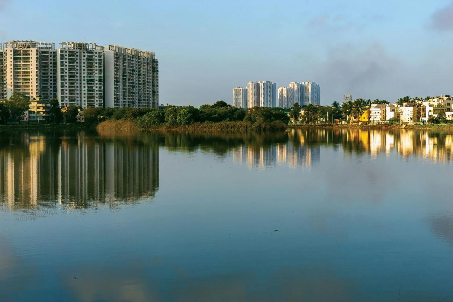 A calm lake in Bangalore with a large apartment complex along its shore. Another apartment complex lies in the distance.