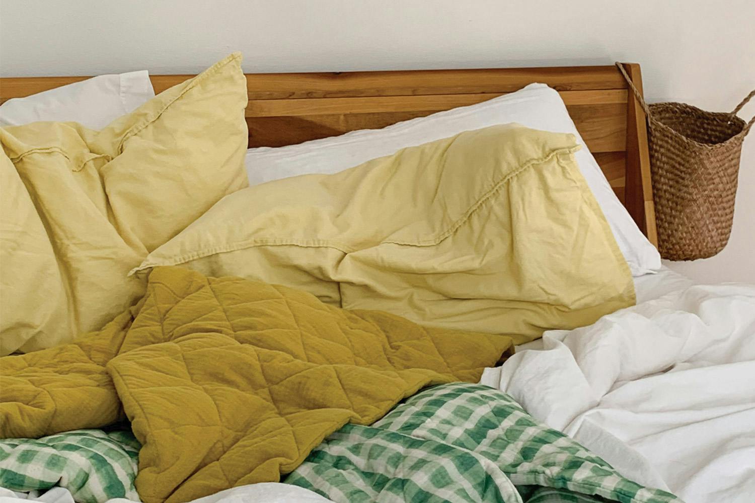 A wooden bed topped with soft-looking yellow, white, and checkered green bed sheets.