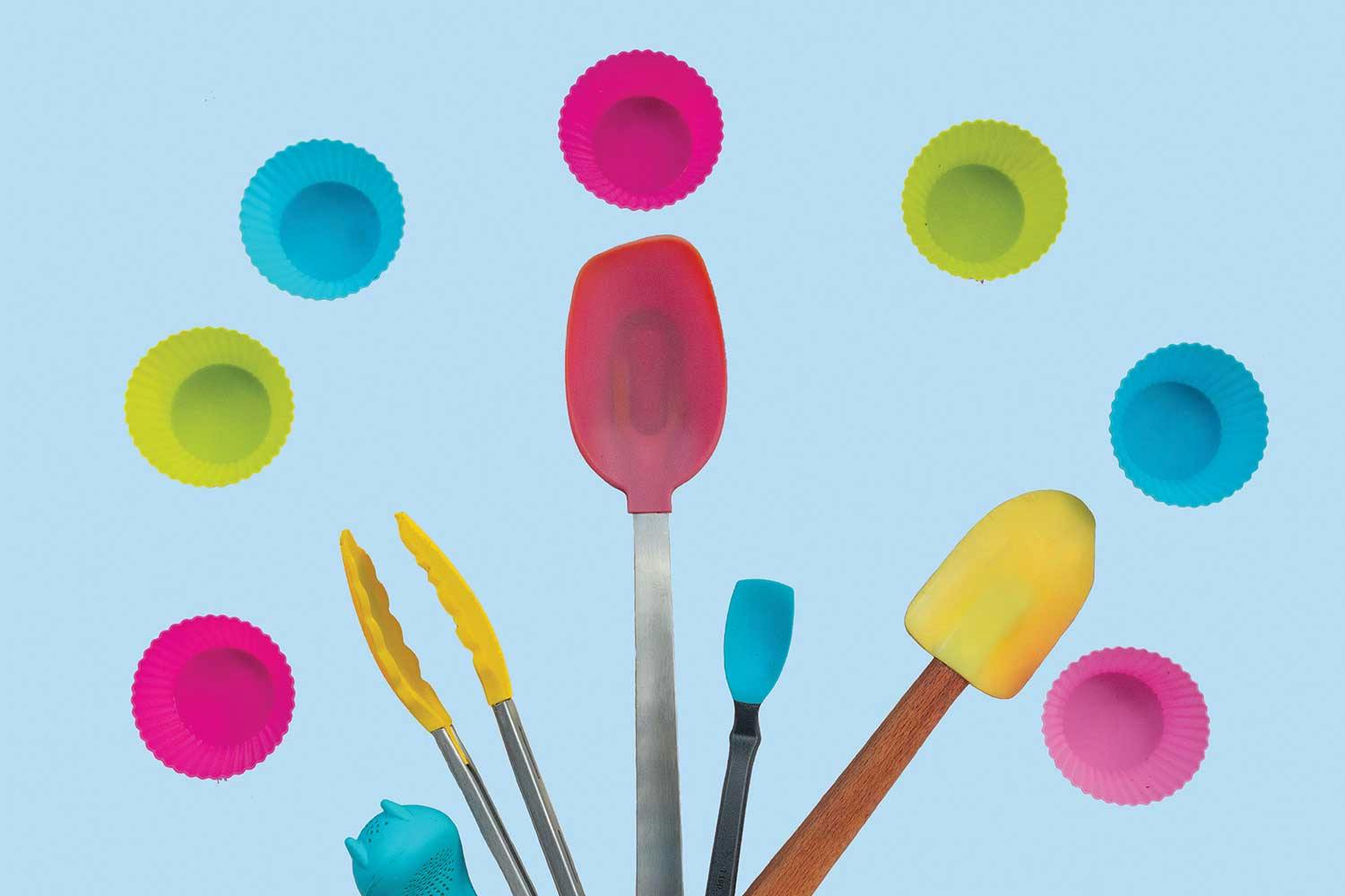 Silicone kitchen tools arranged in a fan shape sit on a blue background, with silicone cupcake liners scattered above them.