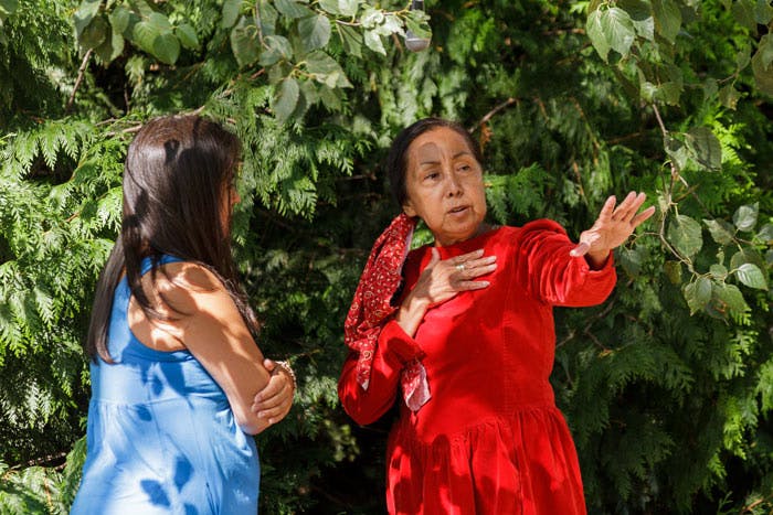 Crystal Smith and Kat Zucomulwut Norris stand in a park talking to each other, as Kat gestures with her left hand.